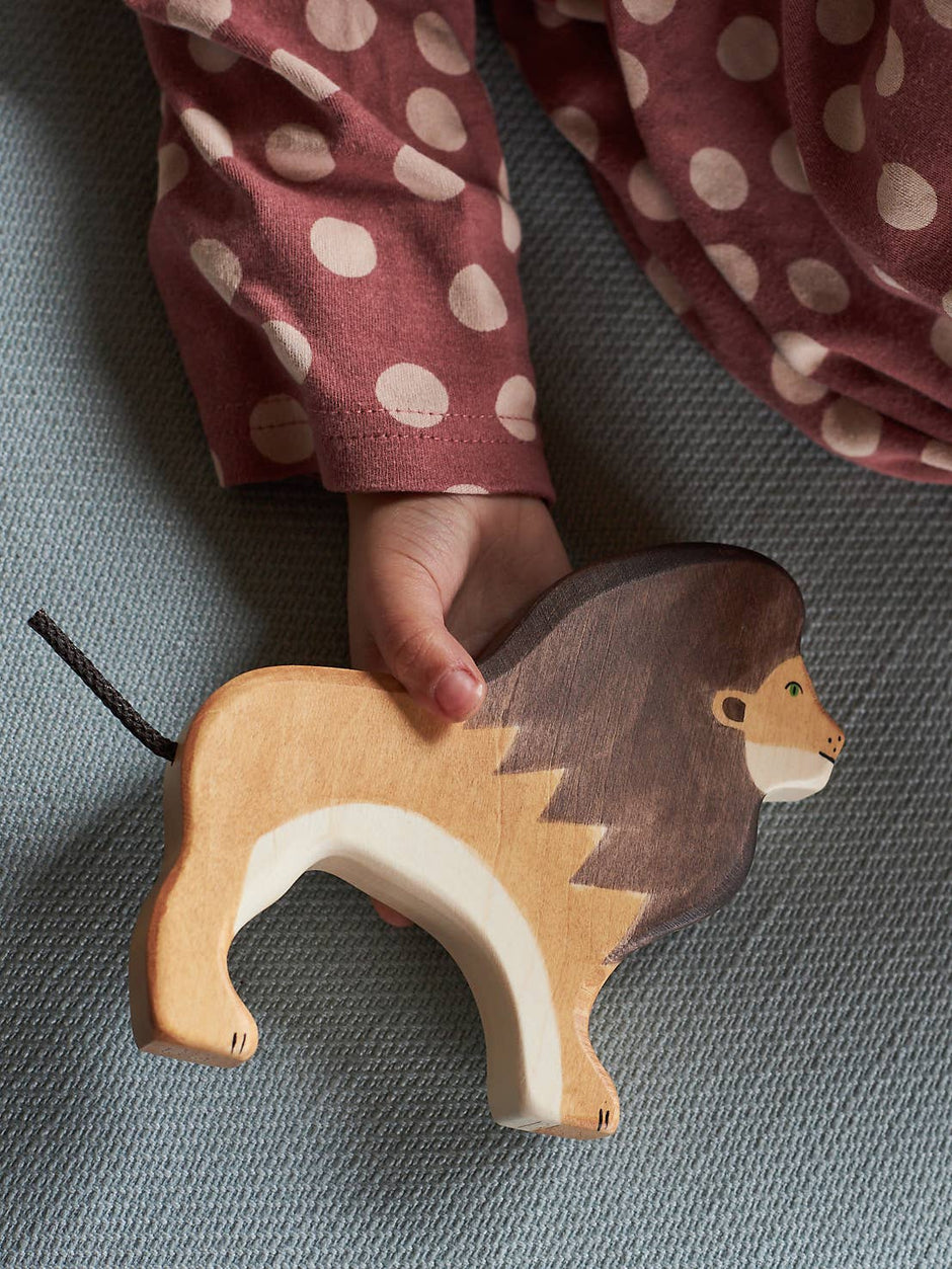 Wooden lion toy held by a child's hand on a textured surface